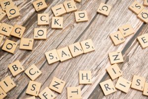 Clean wooden Scrabble tiles spelling "SASS" on rustic wood surface, surrounded by other letter tiles.
