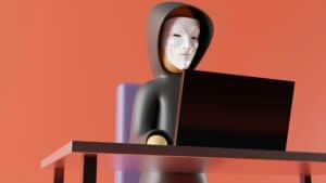 Person wearing a Guy Fawkes mask working on a laptop, symbolizing cybersecurity and hacking prevention.