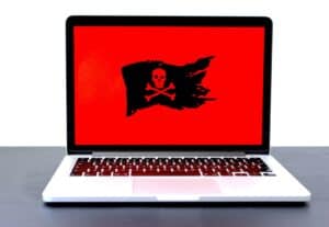 Laptop displaying a red screen with a black pirate flag featuring a skull and crossbones, symbolizing ransomware and cyber threats.