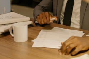 Professional in a business suit reviewing insurance renewal documents at a wooden desk with a white mug and papers.
