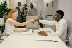 A young woman and a young man shake hands across a conference table in a modern office setting, symbolizing successful onboarding and collaboration.